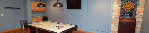 A pool table in a room with wooden flooring and a stone wall.
