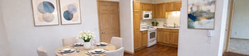 A dining room with a table set for two and a kitchen in the background.