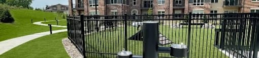 A black metal fence surrounds a grassy area in front of a brick apartment building.