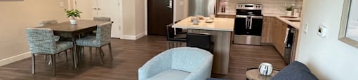 a living room with a couch a table and a chair and a kitchen with a stove and
