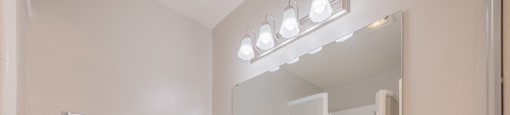 A bathroom with a sink, mirror, and lights above it.