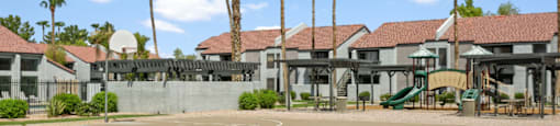 A basketball court surrounded by palm trees and a building in the background.
