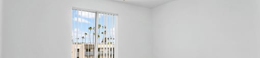 A room with a window overlooking a building with palm trees.