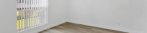 A room with a window covered by white blinds and wooden flooring.