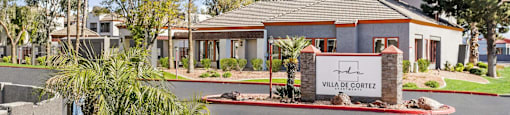 Community entrance with monument sign and palm trees at Villa de Cortez Apartments, Phoenix, AZ 85033