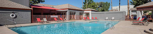 A pool with red sun loungers and a building in the background.