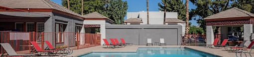 A pool surrounded by red lounge chairs and palm trees.