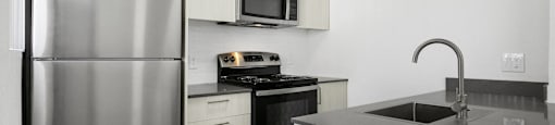 A modern kitchen with a stainless steel refrigerator and black countertops.