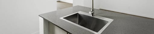A modern kitchen with a stainless steel sink and a white wall.