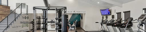 a gym with cardio equipment and weights on the floor and a staircase