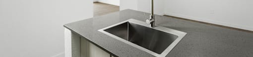 A modern kitchen with a stainless steel sink and a white wall.