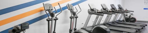 a row of exercise machines in front of a white wall with blue and yellow stripes