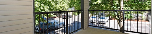 A balcony with a black railing and a view of a parking lot and trees.
