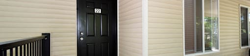 A black door with a glass window is on the left side of a tan building.