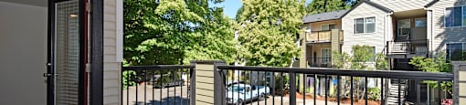 A balcony with a black railing and a view of a parking lot and other houses.