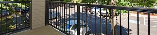 A balcony with a black railing and a view of a parking lot and trees.