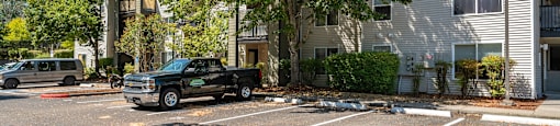 A black pickup truck is parked in a parking lot in front of a two-story apartment building.