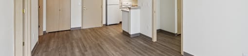 an empty living room with a kitchen in the background