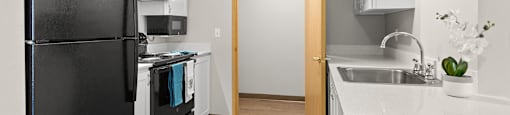 Apartments in Federal Way - Meridian Court - White Countertops, White Cabinets, Wood-Style Flooring, and Black Appliances