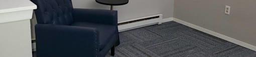 A blue chair is in front of a white wall with two framed pictures on it.