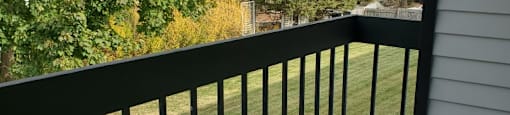 A black railing on a white house overlooks a green lawn.