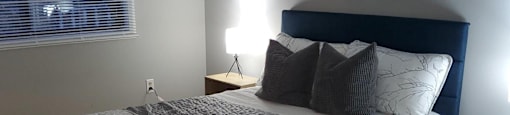 A bed with a grey and white comforter and a black headboard with a painting above it.