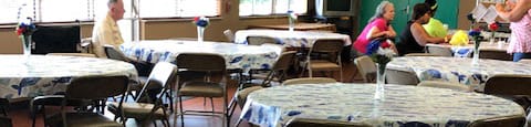 tables and chairs beside large windows in community room at Deedco Gardens