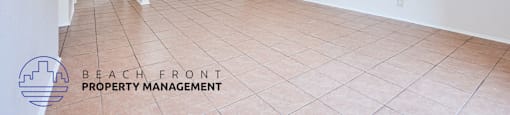 A spacious room with tiled flooring and a logo for Beach Front Property Management in the corner.