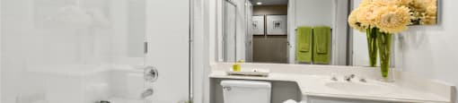 Spacious bathroom with oval soaking tub with glass enclosure, cultured marble vanity, glass shower, and built-in vanity at The Lanesborough Apartments in Houston.