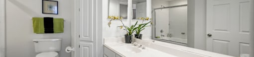 Spacious bathroom with oval soaking tub with glass enclosure, cultured marble vanity, glass shower, and built-in vanity at The Lanesborough Apartments in Houston.