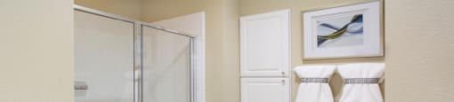 Luxury bathroom with tiled floors, glass shower, linen closet, and white cabinets in at TurtleCreek apartments in West Des Moines, Iowa
