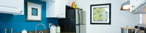 Sienna Apartments, kitchen area with a dishwasher a stainless steel fridge white cabinets and blue backsplash wall