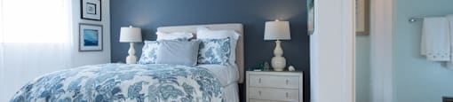 Sienna apts bedroom with a dark teal wall a bed placed int he middle of two white nightstands with blue flower bedspread.