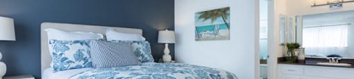 Sienna apts bedroom with a dark teal wall a bed placed int he middle of two white nightstands with blue flower bedspread.