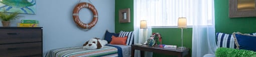 Sienna apts with a green accent wall with two twin beds adorned with striped bedspreads and a brown dresser in the corner
