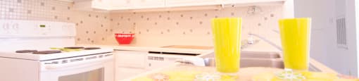 a white kitchen with yellow glasses on the counter