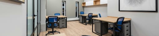 A room with wooden floors and white walls has several desks and chairs.