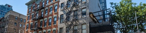 A modern building with a glass facade is situated next to a traditional brick building with a fire escape.
