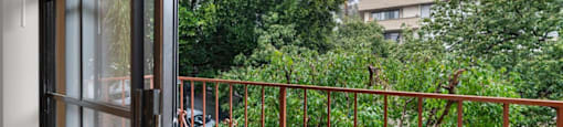 A balcony with a metal railing and a view of a green tree and a building.