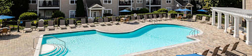 a swimming pool with chairs and umbrellas in front of an apartment building