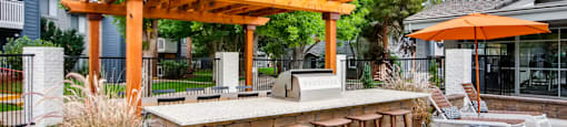 A wooden pergola with a bar and stools is surrounded by greenery.