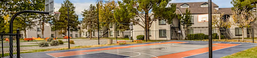 a basketball court with trees and apartments in the background