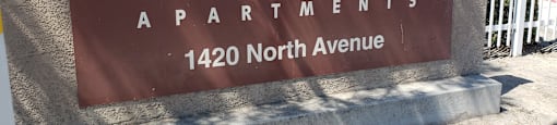 A brown sign that says Kings Manor Apartments stands on a sidewalk.