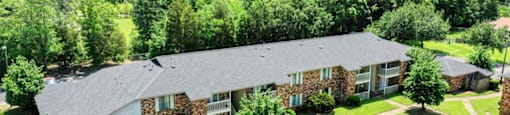 A large house with a grey roof surrounded by a green lawn and trees.