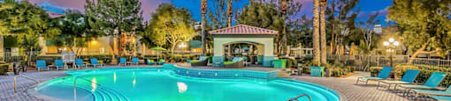 a swimming pool with chairs and trees around it at night at Mirasol Apartments, Nevada, 89119