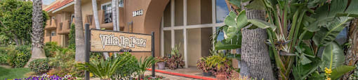 a building with a sign in front of a flower garden at Villa La Paz Apartments, Bellflower