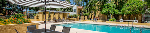 a swimming pool with a table and chairs under an umbrella at Ascent on Peoria Apartments, Arizona