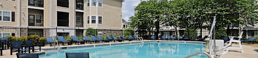A swimming pool surrounded by chairs and trees in front of a building.