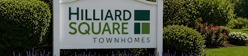 A sign for Hilliard Square Townhomes is surrounded by flowers and greenery.
