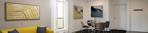 A living room with a yellow couch and a painting on the wall.
